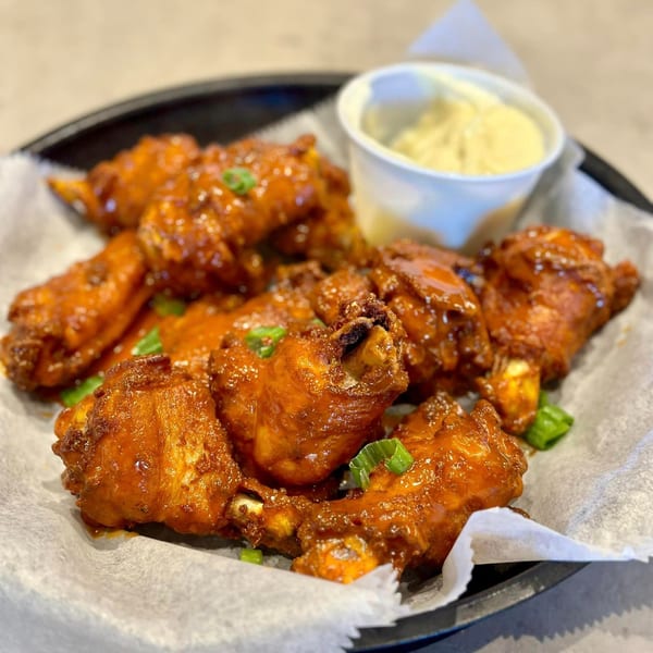 Philly Philly Cheesesteaks' buffalo wings, glistening with sauce and garnished with green onions, served with a side of dip.