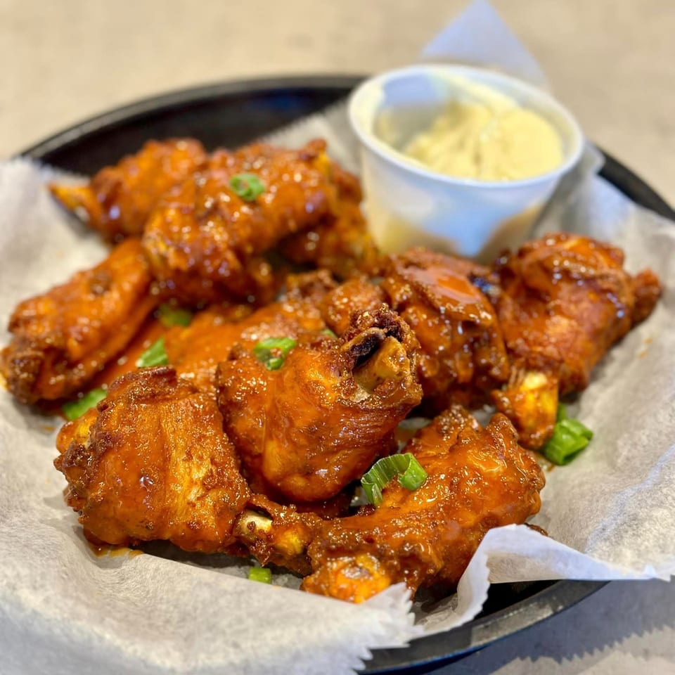 Philly Philly Cheesesteaks' buffalo wings, glistening with sauce and garnished with green onions, served with a side of dip.