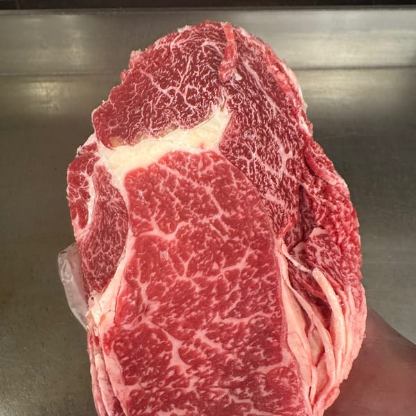 A large, raw cut of marbled red beef, likely for cheesesteaks, held over a metal surface.