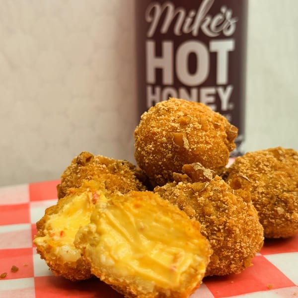 Golden-fried mac and cheese bites on a red and white checkered paper, with a Mike's Hot Honey bottle in the background.