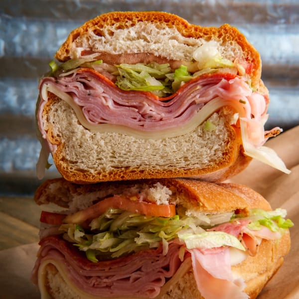 A large Philly Philly Cheesesteaks Italian hoagie, cut in half, revealing layers of meat, cheese, and vegetables.