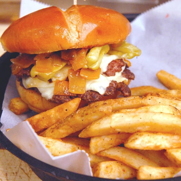 Philly cheesesteak sandwich with melted cheese, peppers, onions, and a side of fries.