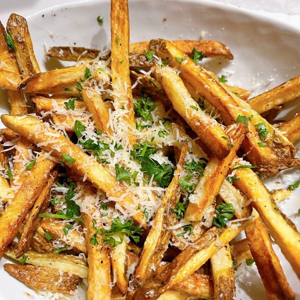 Golden-brown fries topped with grated Parmesan cheese and fresh parsley in a white bowl.