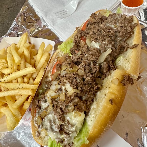 A Philly Philly Cheesesteak with steak, onions, lettuce, tomato, and cheese, served with fries.